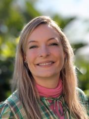 Dr Lexie Prokopuk smiling in front of greenery in a green and pink dress.