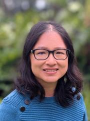 Dr Hsiu-Wen Chan standing in front of greenery in a green jumper with black buttons on the side.