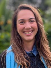 UQ's Leticia Watanabe Ribeiro standing in front of greenery in a blue scarf and jumper.