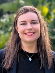 UQ's Paige Booth standing in front of greenery in black blazer.