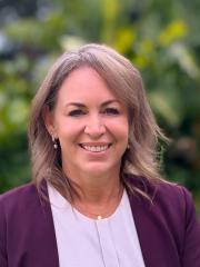 UQ's Sandra Comer standing in front of greenery in a purple blazer.