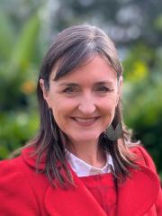 UQ's Sarah Kell standing in front of greenery in a red coat.