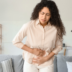 Woman with menstrual pain standing at home holding her stomach with a white clock showing 9am in the background. 