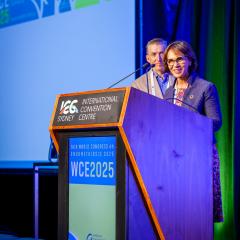 Prof Gita Mishra and Prof Jason Abbott standing at a lectern with a blue light and screen behind them at the World Congress on Endometriosis event in Sydney. 