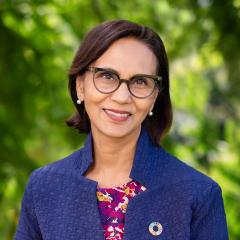 UQ's Professor Gita Mishra standing in front of green plants in a navy jacket with UN Sustainable Development pin.