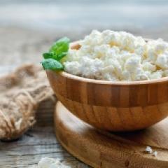 Wooden bowl filled with cottage cheese on top of a wooden board