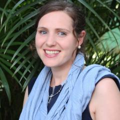 Dr Jane Fox smiling and standing in front of greenery wearing a blue scarf.