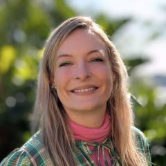 Dr Lexie Prokopuk smiling in front of greenery in a green and pink dress.
