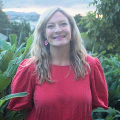 Dr Lexie Prokopuk smiling in front of greenery in a red dress with bright earrings.