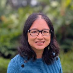 Dr Hsiu-Wen Chan standing in front of greenery in a green jumper with black buttons on the side.