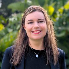UQ's Paige Booth standing in front of greenery in black blazer.