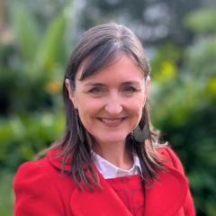 UQ's Sarah Kell standing in front of greenery in a red coat.