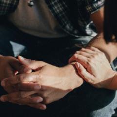 Man clasping hands with woman's hand touching his arm