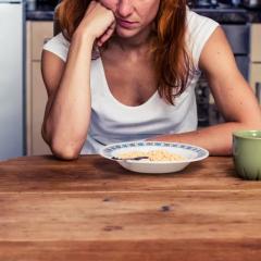 Tired woman staring at bowl of breakfast, cereal and cup on kitchen table